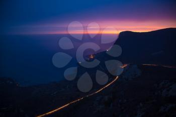 View from the mountain peak on the night city, blue sea and high rocks against beautiful sky. Night colorful mountain landscape. Vacation on seashore. Summer travel in Europe. City lights