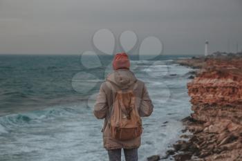Man looking to lighthouse in seaside. Hipsters pictures of sea, sunset stony beach with the lighthouse in the distance