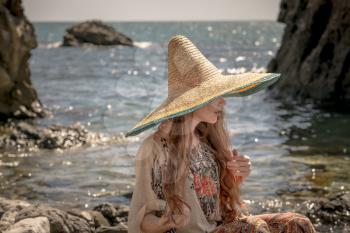 Beautiful boho styled model wearing white top and sombrero posing on the beach in sunlight