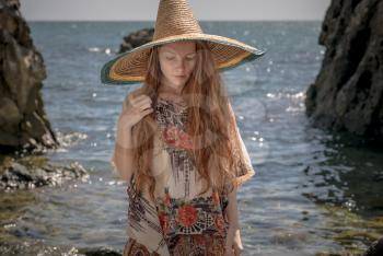 Beautiful boho styled model wearing white top and sombrero posing on the beach in sunlight