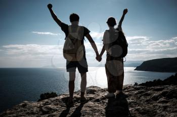 Hikers with backpack standing on top of a mountain with raised hands and enjoying view. team work, man and woman