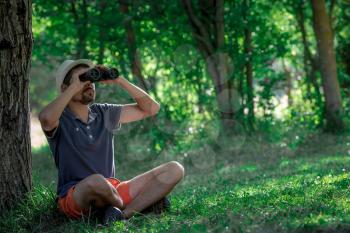 Male hiker looking through binoculars in forest