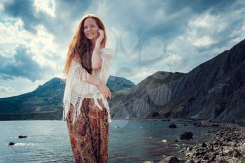 Beautiful boho styled model wearing white crochet swimsuit posing on the beach in sunlight. Red-haired girl with freckles. Crimea, Fox bay, Koktebel