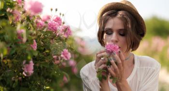 Beautiful young woman with curly hair posing near roses in a garden. The concept of perfume advertising.