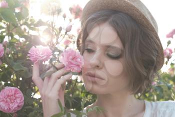 Beautiful young woman with curly hair posing near roses in a garden. The concept of perfume advertising.