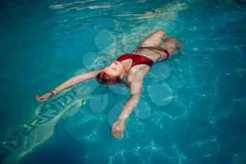 Enjoying suntan and vacation. Colorful portrait of pretty young woman in red swimsuit lying near swimming pool.