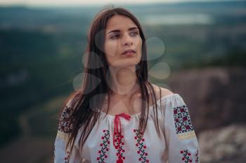 Atractive woman in traditional romanian costume on mountain green blurred background. Outdoor photo. Traditions and cultural diversity