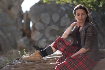 Young woman sitting on cliff and enjoy the view. A girl in a kilt, a Scandinavian mood. Crimea, Mount Cat
