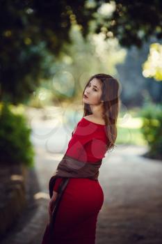 Beautiful girl in a red dress, long dark hair and with Asian appearance walks along the spring park