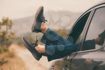 Summer road trip car vacation concept. Woman legs out the windows in car above the road in forest. Conceptual freedom, travel and holidays image with copy space.