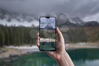 A man makes a photo on a smartphone, beautiful landscape of Lake Carezza with Mount Latemar, Bolzano province, South tyrol, Italy
