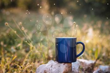Blue mug of hot tea or coffee with milk, outdoor, Concept adventure active vacations outdoor. Summer camping.