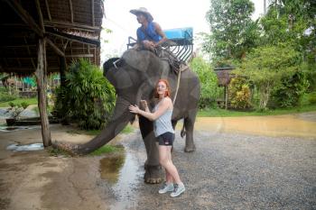 Asian natural scenery. Young red-haired girl feeding an elephant after a walk. Popular attraction in Thailand