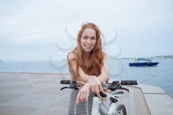 Beautiful woman riding on bike. Lifestyle and health in the city. Cheerful red-haired young woman gets pleasure from walking around the city