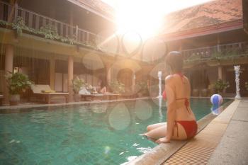 Vacation lifestyle scene of young woman sitting in swimming pool. Weekend and holiday lifestyle concept. soft light at sunset in a hotel in traditional Thai style, rest in an exotic