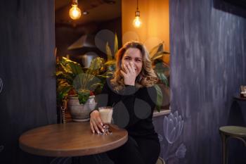 Smiling woman in a good mood with cup of coffee sitting in cafe. dark interior, evening gatherings in a cafe