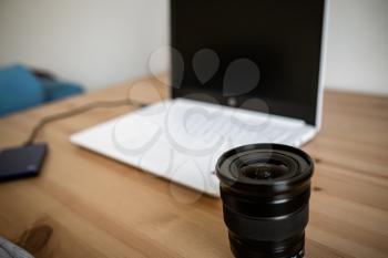 MOSCOW, RUSSIA - 17 MARCH 2019: A DSLR lens of FUjiFILM on a wooden table together with a photo camera, computer. Minimal workspace with Laptop and lens