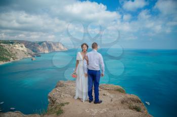 Beautiful smiling young bride and groom walking on the beach, kissing and having fun, wedding ceremony near the rocks and sea. Wedding ceremony on coast of Cyprus