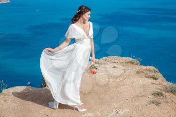 A beautiful bride standing on the coast. The bride in mountains. Wedding. Romantic beautiful bride in white dress posing on the background sea