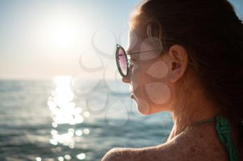Ginger girl with freckles in a bikini looks at a beautiful sunset over the sea. Idea and concept of relaxation, freedom, vacation and happiness