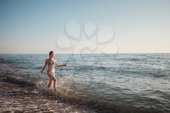 Ginger Girl in a bikini runs along the waves on the beach in summer. Sea vacations concept with copy space.