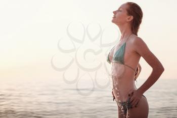 Happy woman wearing bikini is playing and splashing in the sea. Close-up, part of the body of a sexy ginger girl with splashes on the beach.