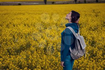 Woman traveler in a blue sweater and jeans in a flowering rapeseed field. Happy beautiful young woman enjoys smell of blooming rapeseed field full of joy and happiness. Concept of freedom