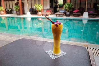 fresh tropical smoothie or mango juice in a tall glass on the background of the pool