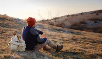 A young man sitting in spring mountains at sunset and enjoying view of nature. Mountain and coastal travel, freedom and active lifestyle