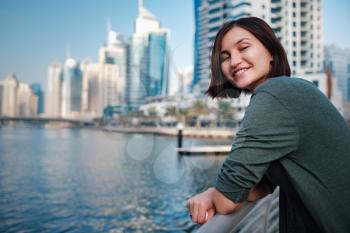 Happy young female traveler in the big city of Dubai, famous place Dubai marina. Luxury and comfortable tourism season in United Arab Emirates.