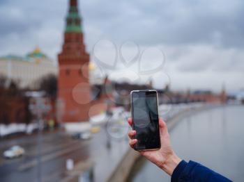 Female tourist hand taking pictures on mobile phone on the background of Moscow Kremlin, Russia, close-up