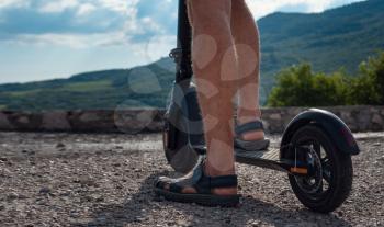 Young man riding an electric scooter on mountain range. Close up of man riding black electric kick scooter at beautiful landscape. Ecological transportation concept