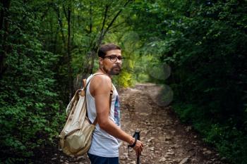 Portrait of a man hiker walking on the trail in the woods. Strong sporty traveling male with backpack on a forest background.