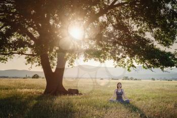 Attractive woman practices yoga in nature in summer. Healthy lifestyle. Concept of calm and meditation.