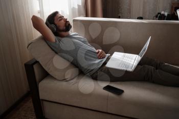 Man on sofa with headphones and notebook at home. young hipster wear headphones study online watching webinar podcast on laptop listening learning education course or music, elearning concept