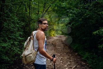 Portrait of a man hiker walking on the trail in the woods. Strong sporty traveling male with backpack on a forest background.