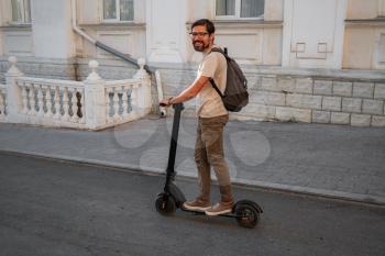 fun driving electric scooter through the city. A hipster man enjoys a walk through the city during the summer sunset. The idea and concept of ecology, style and fun moving around the city