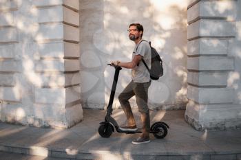 fun driving electric scooter through the city. A hipster man enjoys a walk through the city during the summer sunset. The idea and concept of ecology, style and fun moving around the city