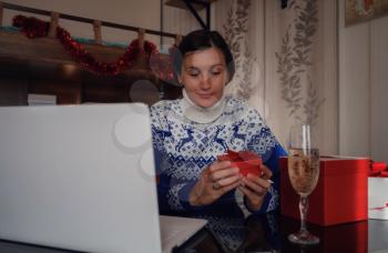 Christmas online congratulations. Smiling asian woman in blue sweater using computer for video call friends and parents. Emotional face.