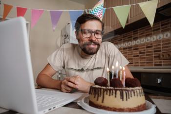 Man celebrating birthday online in quarantine time. Guy celebrating his birthday , blowing out the candle on the birthday cake and making video call. Coronavirus outbreak 2020.