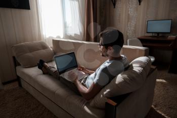 Remote Job. Man Working On Laptop Sitting On Sofa At Home. Copy Space For Text. freelancer hipster works from home, studying or communicating with partners