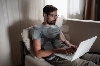 Remote Job. Man Working On Laptop Sitting On Sofa At Home. Copy Space For Text. freelancer hipster works from home, studying or communicating with partners