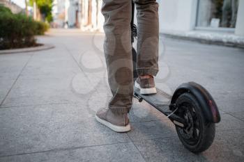 Close up of man riding black electric kick scooter at cityscape at sunset. Electric urban transportation concept image