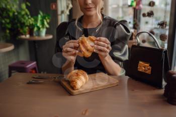 Woman holding a mug of coffee and a croissant in her hands in coffee shop. Breakfast menu in the morning time.