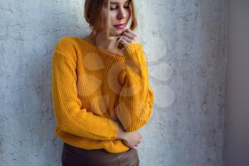 Young woman in a yellow sweater posing against the wall. idea and concept of comfort and tenderness