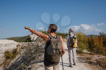 Two Hikers with Backpacks and other climbing Gear staying on top of Rock. man pointing with his hand discussing route. Plan, vision and mission concept.