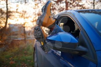 Woman feet in trendy yellow hiking boots on car door. Feet outside the window at sunset forest. The concept of freedom of movement. An autumn weekend in nature.