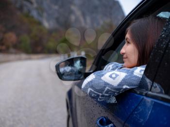 Asian young hipster woman traveling on car vacation. Autumn drive. The rain is falling. The concept of freedom of movement. Fall weekend in the mountains.