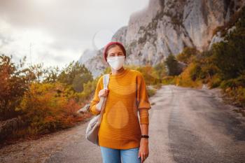 A young woman with a protective face mask is on a walk in nature and she is thinking about when the quarantine ends - topic of corona virus - COVID 19. Wanderlust photo series.
