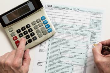 Male caucasian hand holding pen above USA tax form 1040 for year 2015 and calculator illustrating completion of tax forms for the IRS